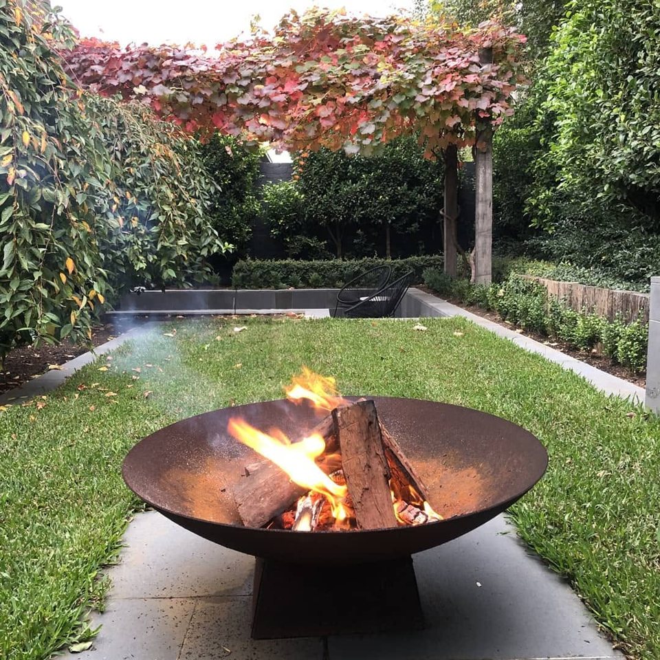 Fire bowl alight beside the lawn with the autumn ornamental grape over the fence