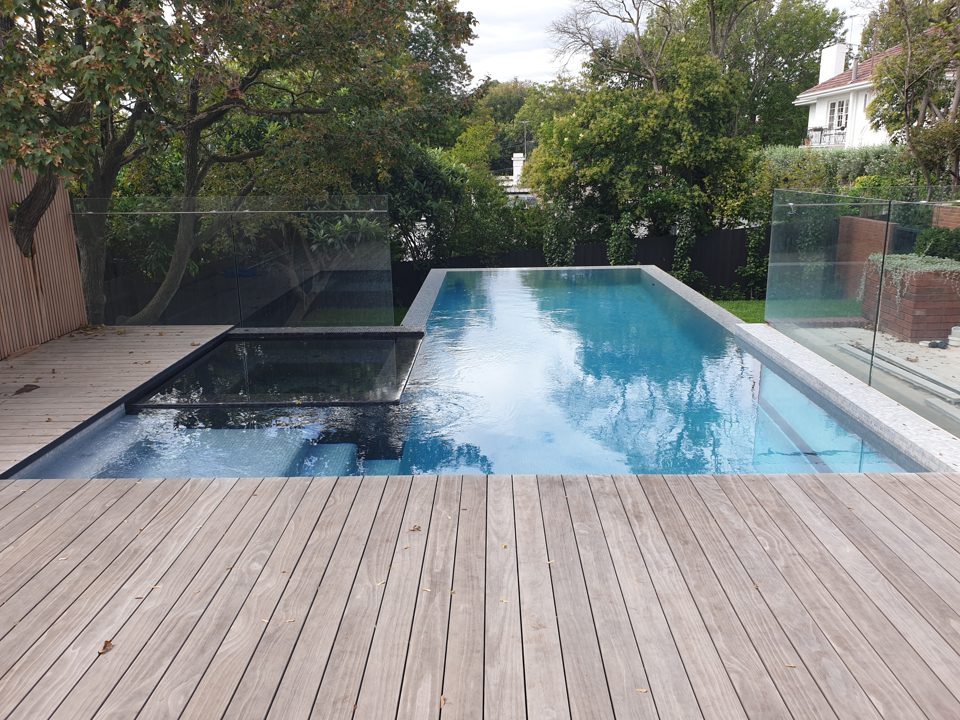 Swimming pool and timber deck enclosed by brick walls and glass fencing