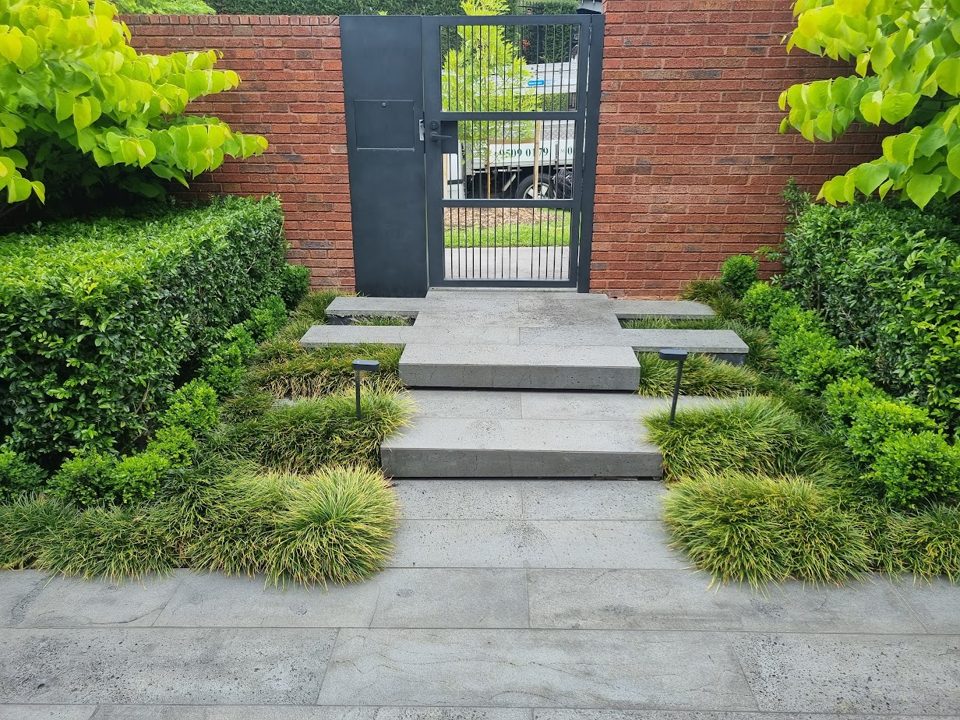 Bluestone entry steps between clipped hedges and a steel gate