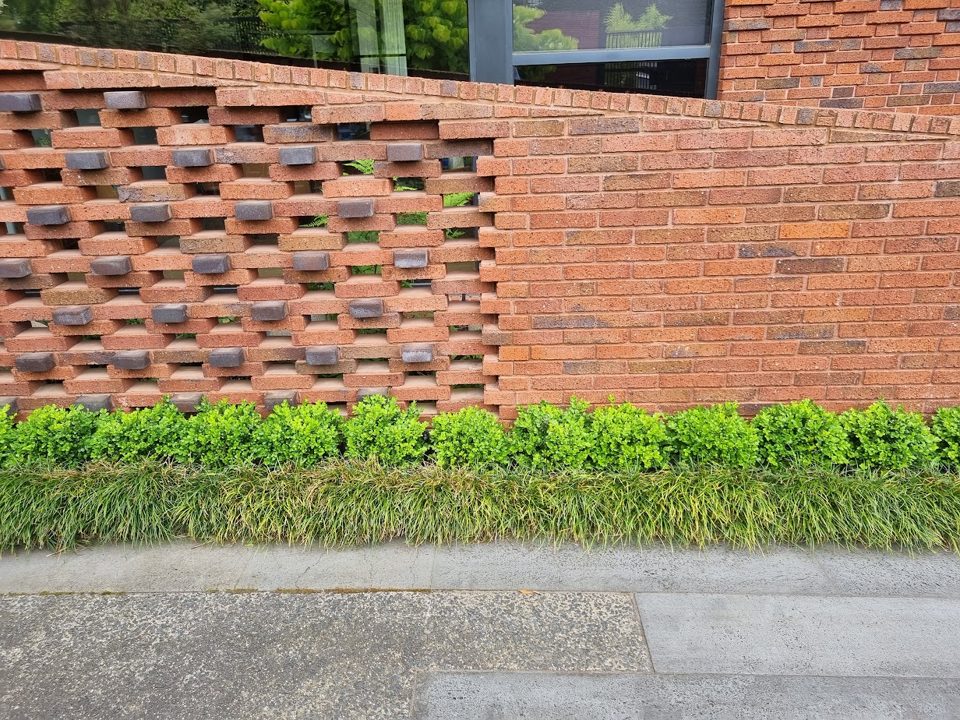Hit-and-miss brick screen wall above a clipped hedge